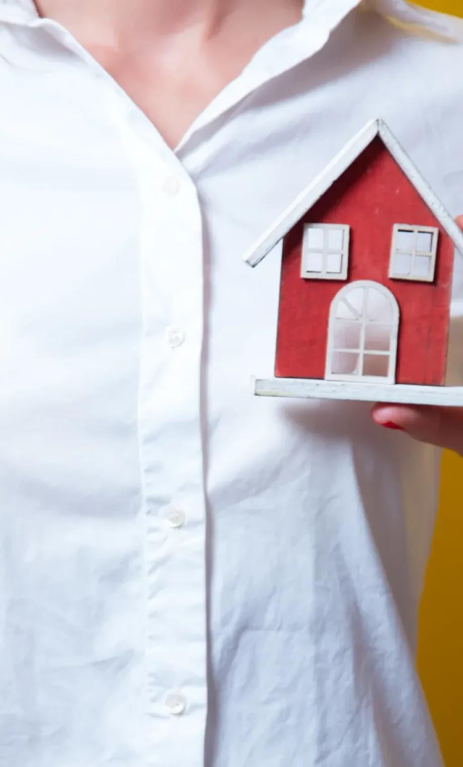 photo of beautiful young woman with house shaped toy on the yellow background